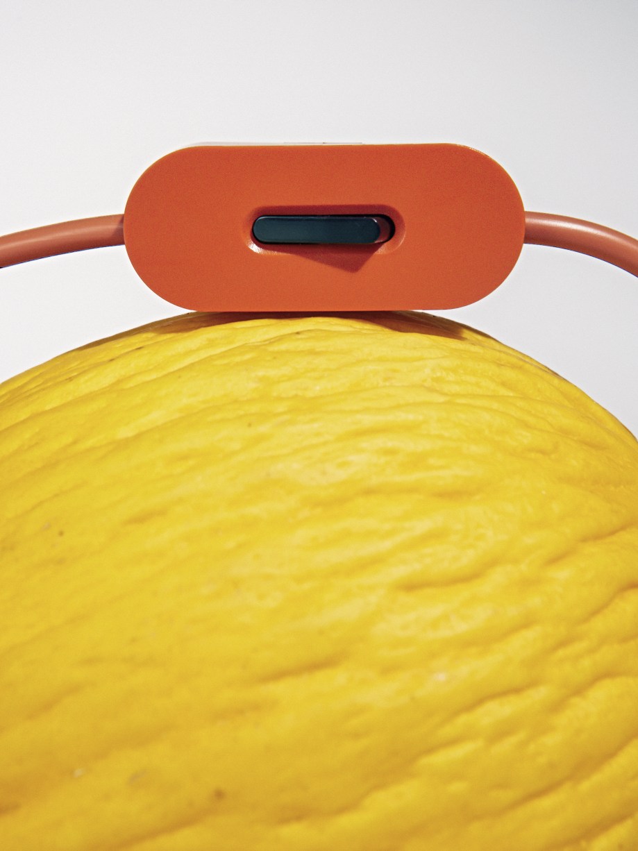 Detailaufnahme der Bilboquet Tischleuchte von Flos in Leinenoptik, mit orangefarbenem Schalter auf gelbem Hintergrund.