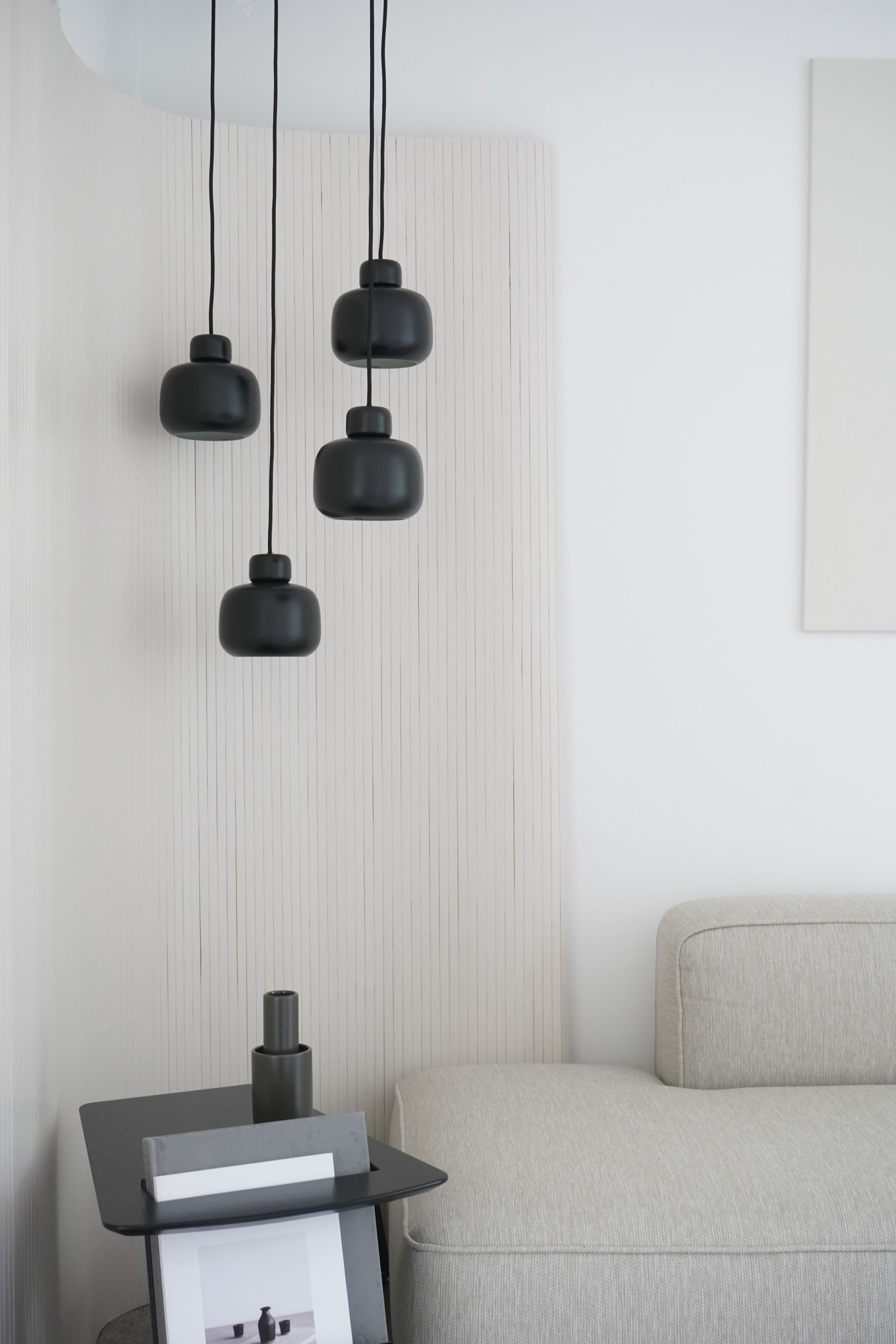 Nahaufnahme von drei kleinen, schwarzen Stone Pendant Pendelleuchten von Woud über einem Beistelltisch und Sofa.