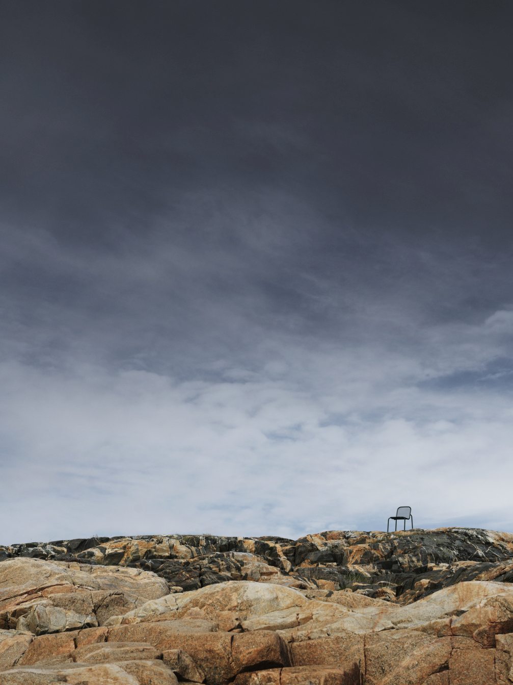 Vig Chair Stuhl von Normann Copenhagen auf Felsen unter bewölktem Himmel, Outdoor Möbel.
