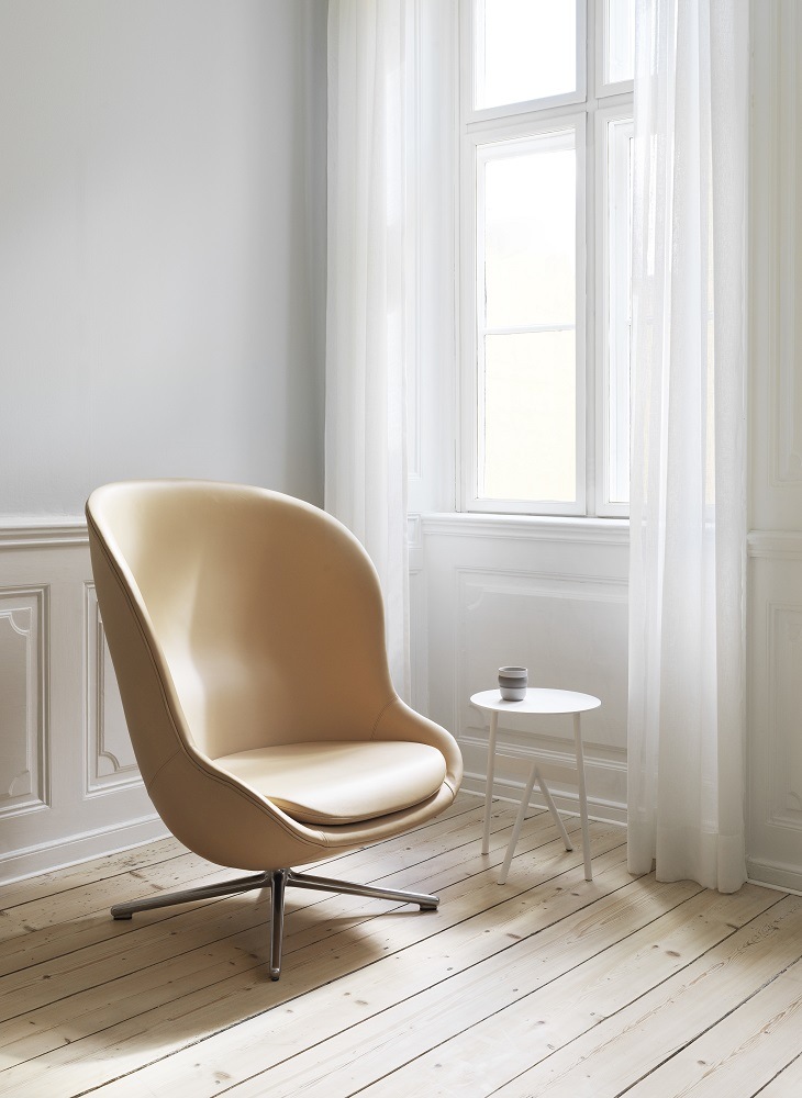 Beiger Hyg Lounge Sessel mit Drehgestell von Normann Copenhagen vor Fenster mit Vorhängen.
