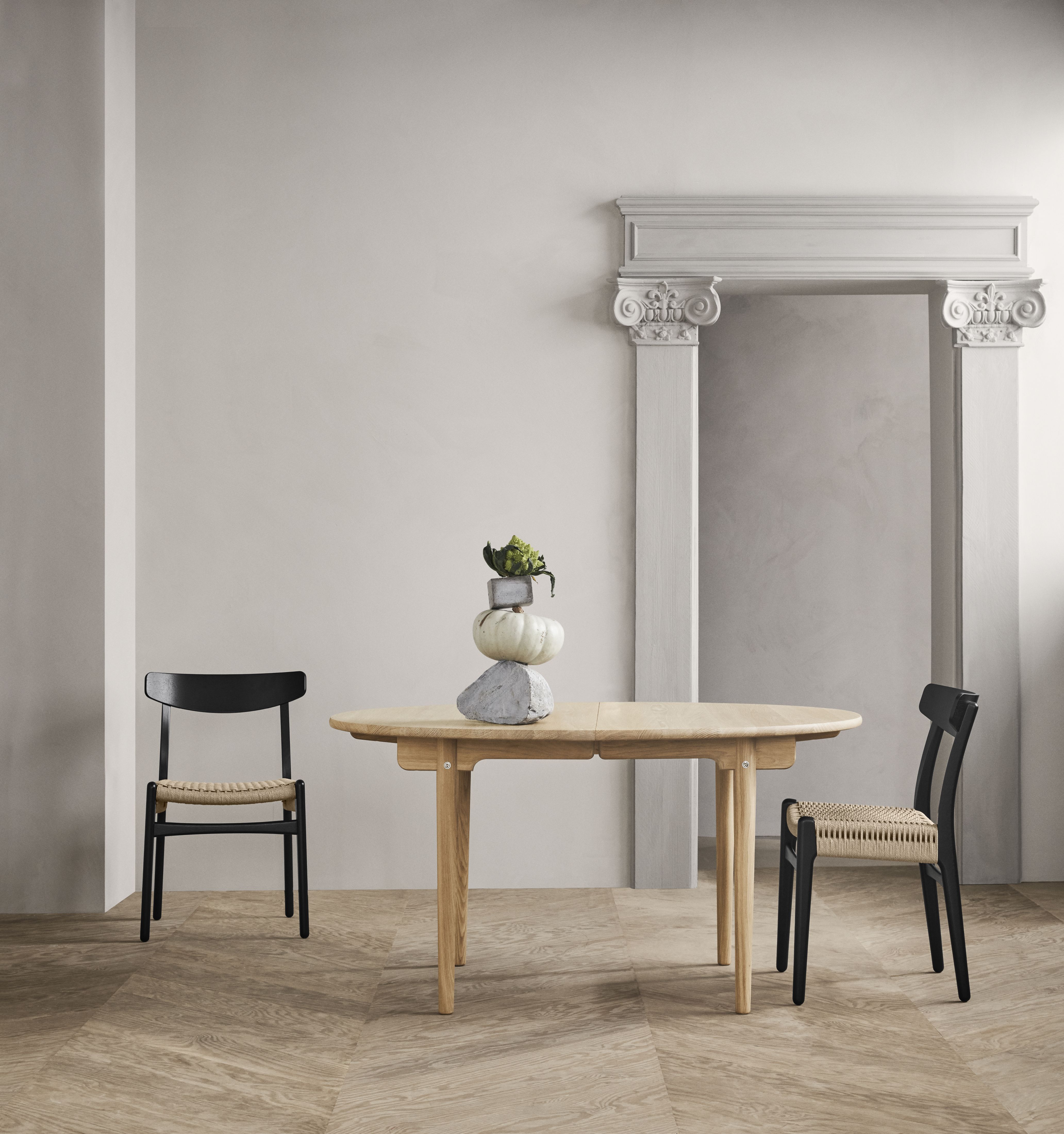 CH337 Esstisch oval ausziehbar von Carl Hansen mit zwei schwarzen Stühlen und Dekoration.