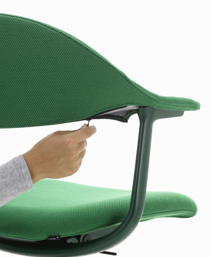 Detailaufnahme: Hand öffnet Reißverschluss am grünen Mynt Bürodrehstuhl von Vitra, Fokus auf Rückenlehne und Sitzfläche.