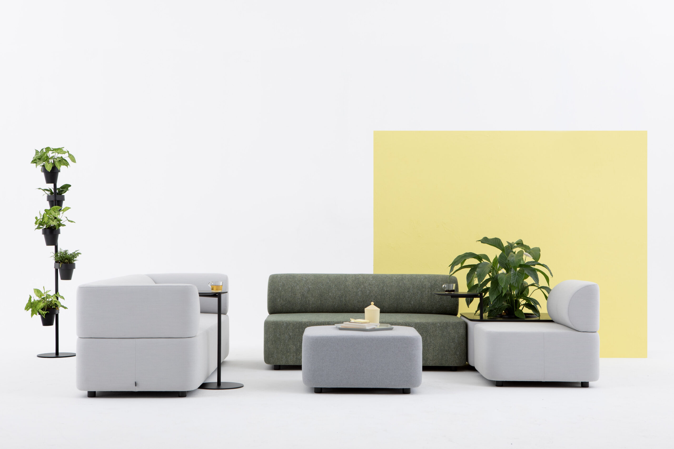 Mezza Sofa von Cascando, modulares Sitzelement in Grau und Grün mit Pflanzen und Beistelltischen.