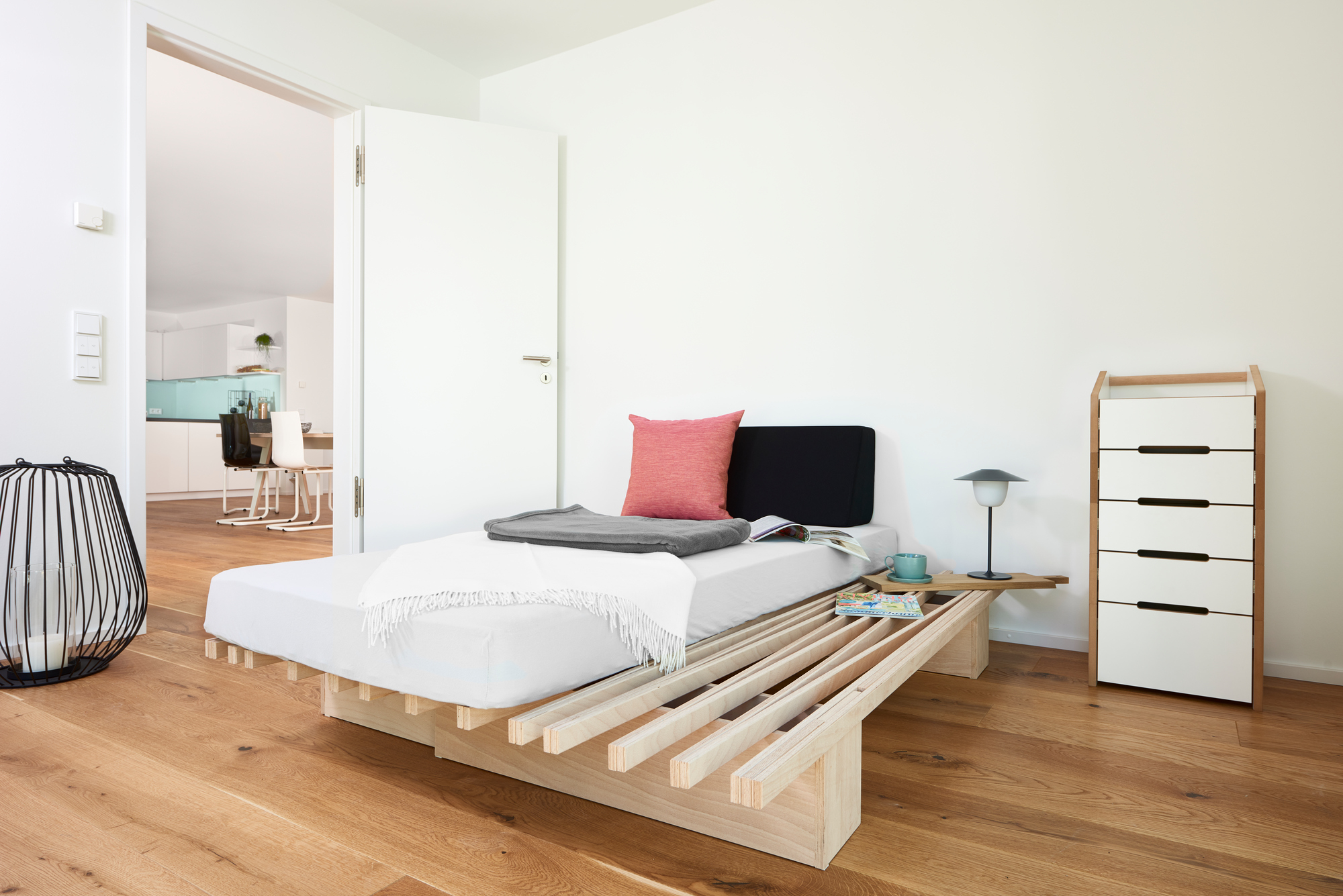 V Bett von Tojo, minimalistisches Einzelbett aus Holz mit Matratze, Kissen und Nachttisch im Schlafzimmer.