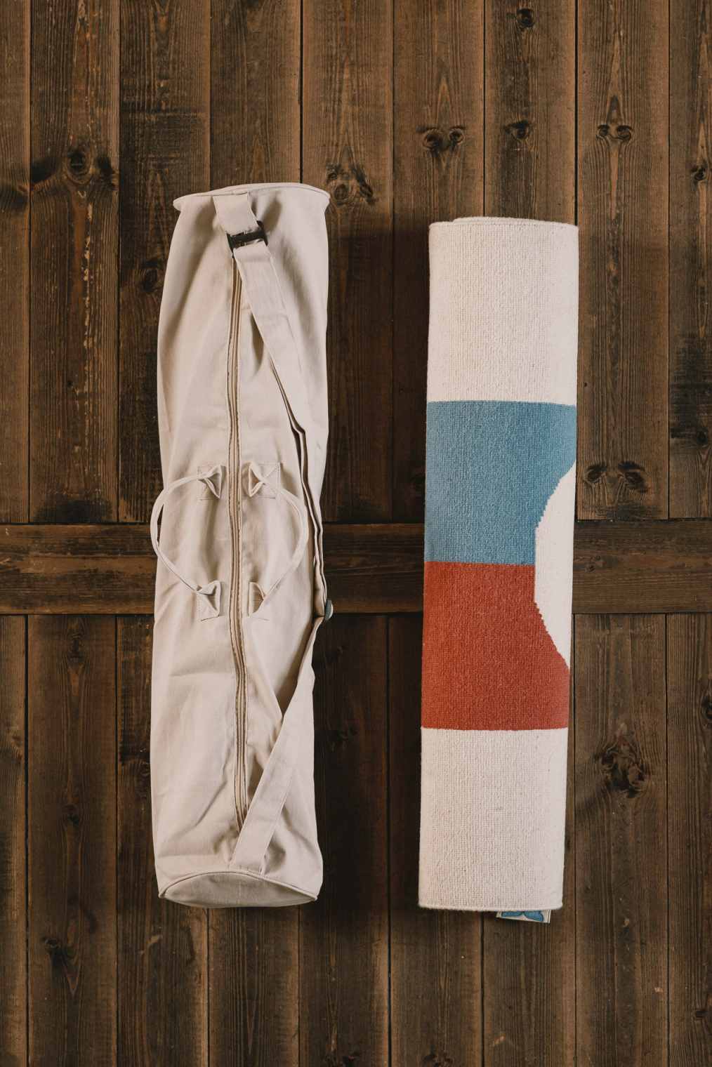 Bela Teppich von Designercarpets, zusammengerollt mit Tragebeutel an einer Holzwand, modernes Wohnaccessoire für stilvolles Ambiente.