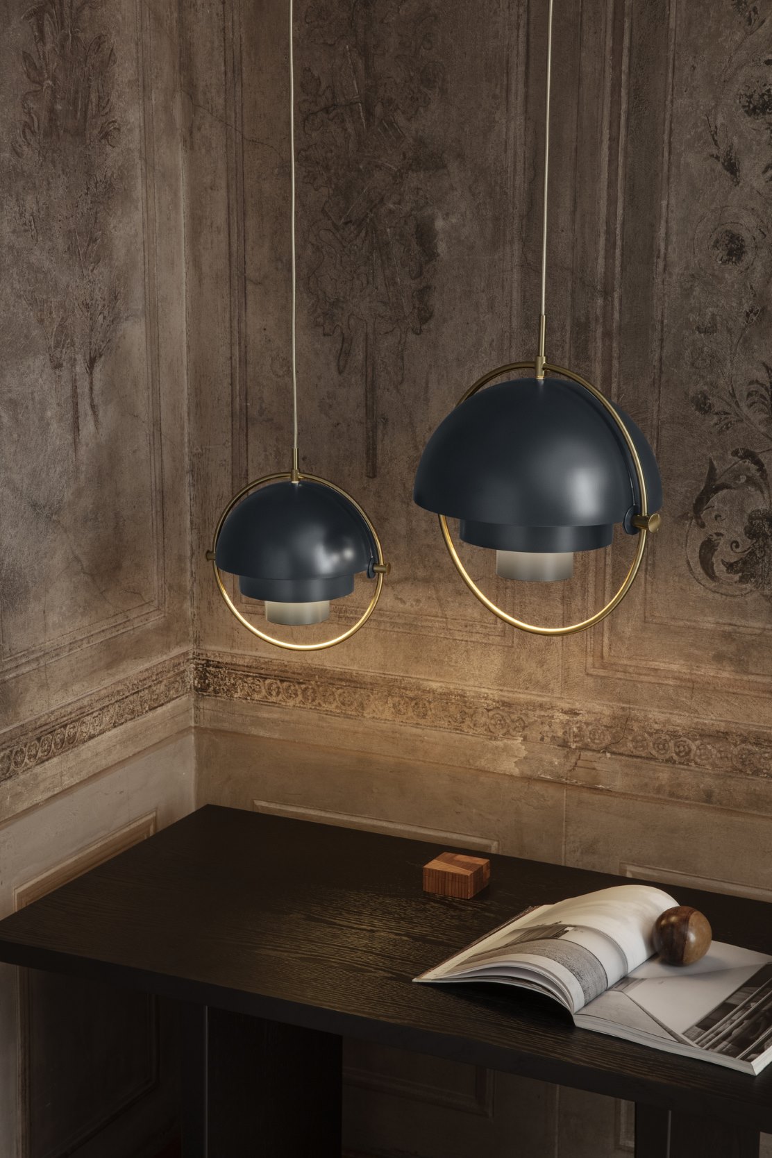 Zwei moderne Pendelleuchten in Dunkelblau mit goldenen Akzenten über einem dunklen Holztisch.