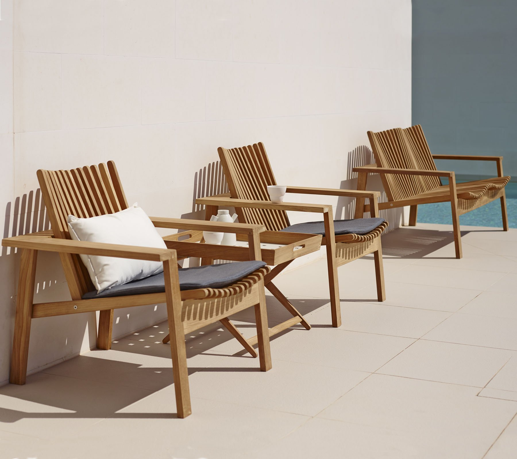 Drei Cane-Line Amaze Outdoor Loungesessel aus Teakholz mit Kissen auf einer Terrasse.