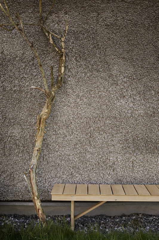Mogensen Bank Outdoor von Carl Hansen & Søn vor Reetdach und Baum im Garten.