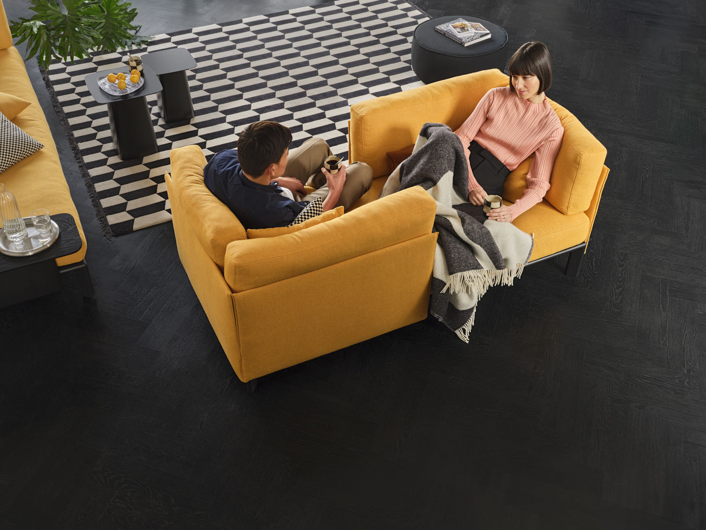 Vitra Anagram Panel 110 cm: Zwei Personen entspannen auf einem gelben Designersofa mit Decke.