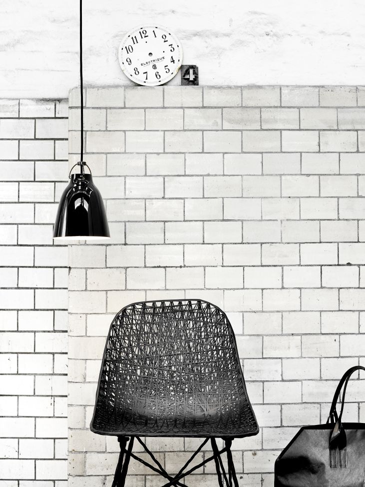 Schwarze Caravaggio Pendelleuchte von Fritz Hansen über einem schwarzen Design-Stuhl vor einer weißen Ziegelwand.