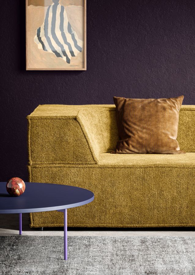 Nahaufnahme des Trio Sofa Modulsofas in Senfgelb mit Kissen und blauem Beistelltisch vor lila Wand.
