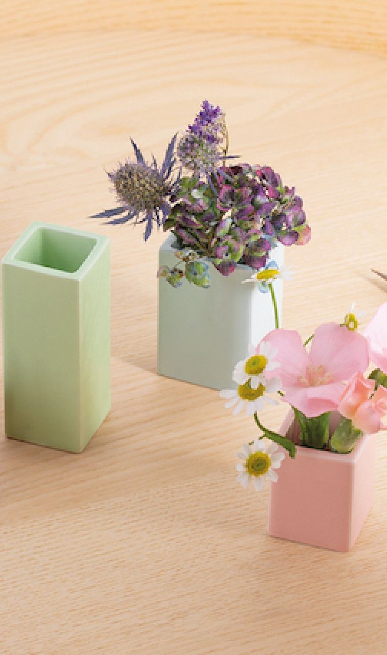 Drei kleine, pastellfarbene Keramikvasen mit Blumen auf einem Holztisch, Dekoration für Zuhause.