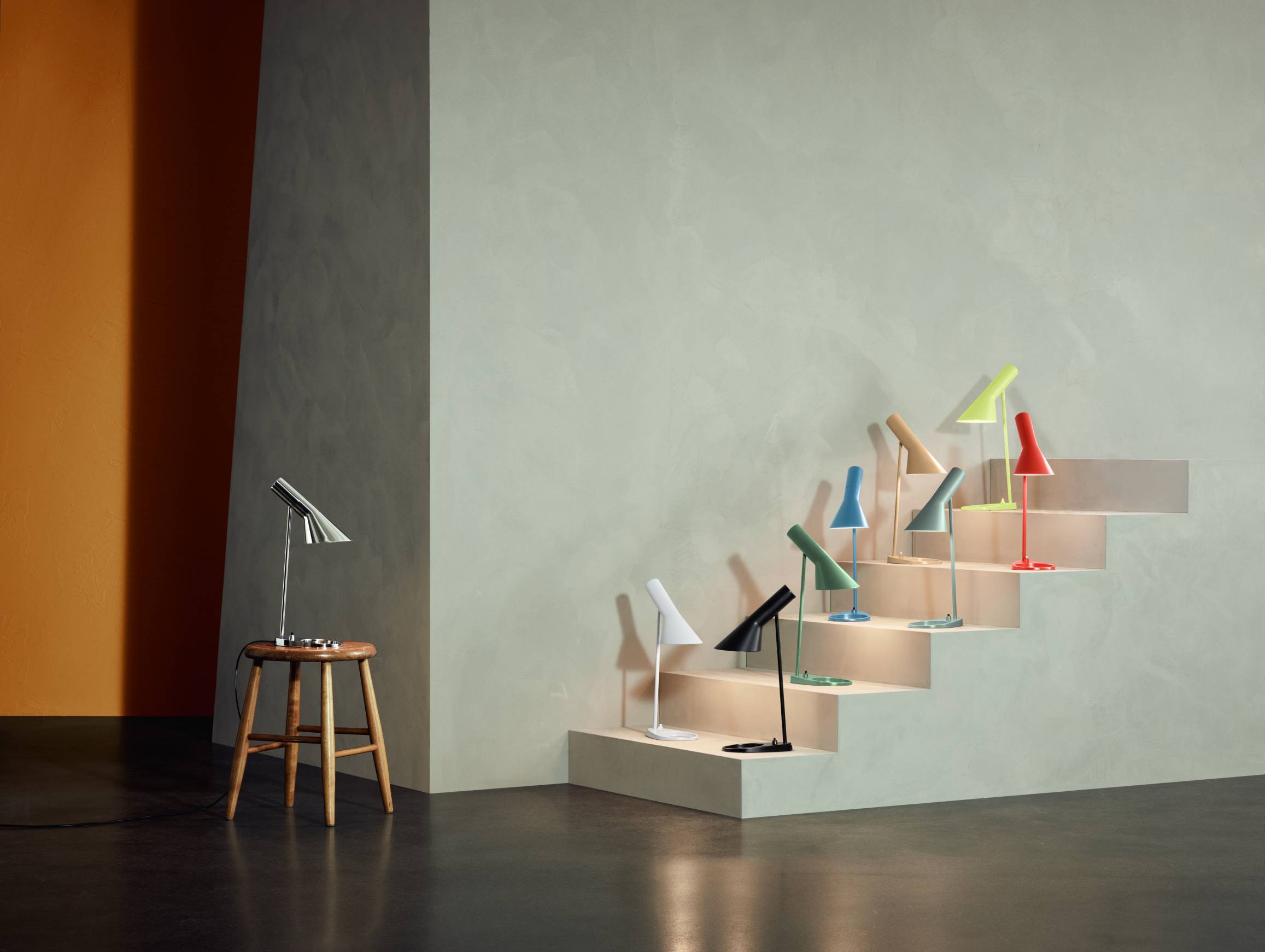 AJ Tischleuchten von Louis Poulsen in verschiedenen Farben auf einer Treppe und einem Hocker.