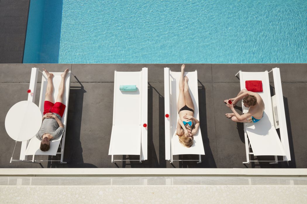 Draufsicht: Menschen entspannen auf weißen Sonnenliegen am Pool, mit Handtüchern und Beistelltisch.