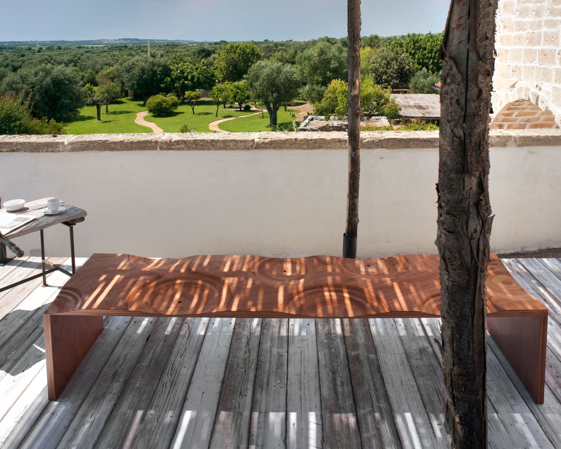 Casamania Horm Ripples Bank für den Außenbereich aus Holz auf einer Terrasse mit Holzboden.
