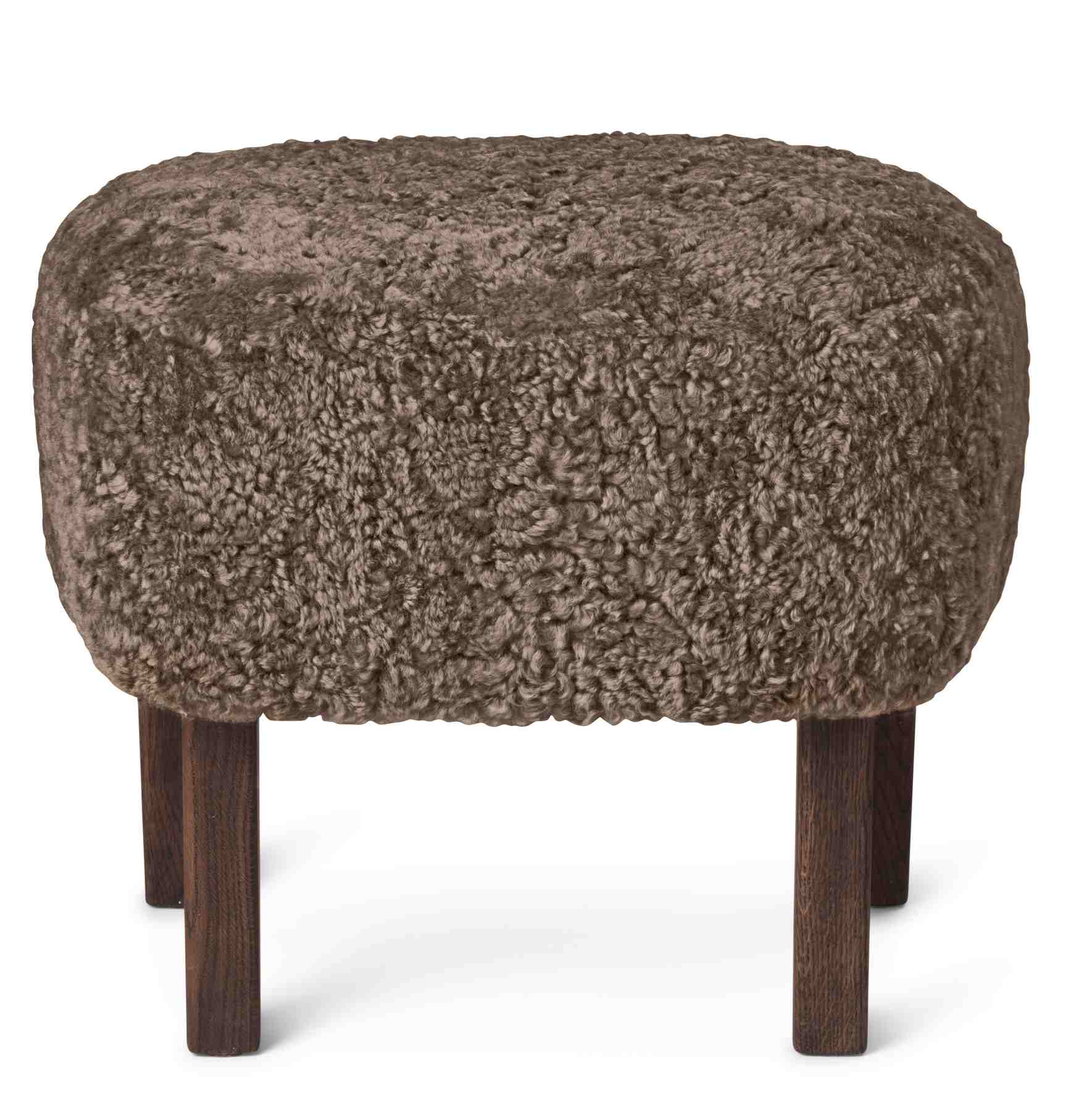 Ingeborg Ottoman Audo: Gepolsterter Hocker mit braunem Schaffellbezug und dunklen Holzbeinen, freistehend auf weißem Hintergrund.