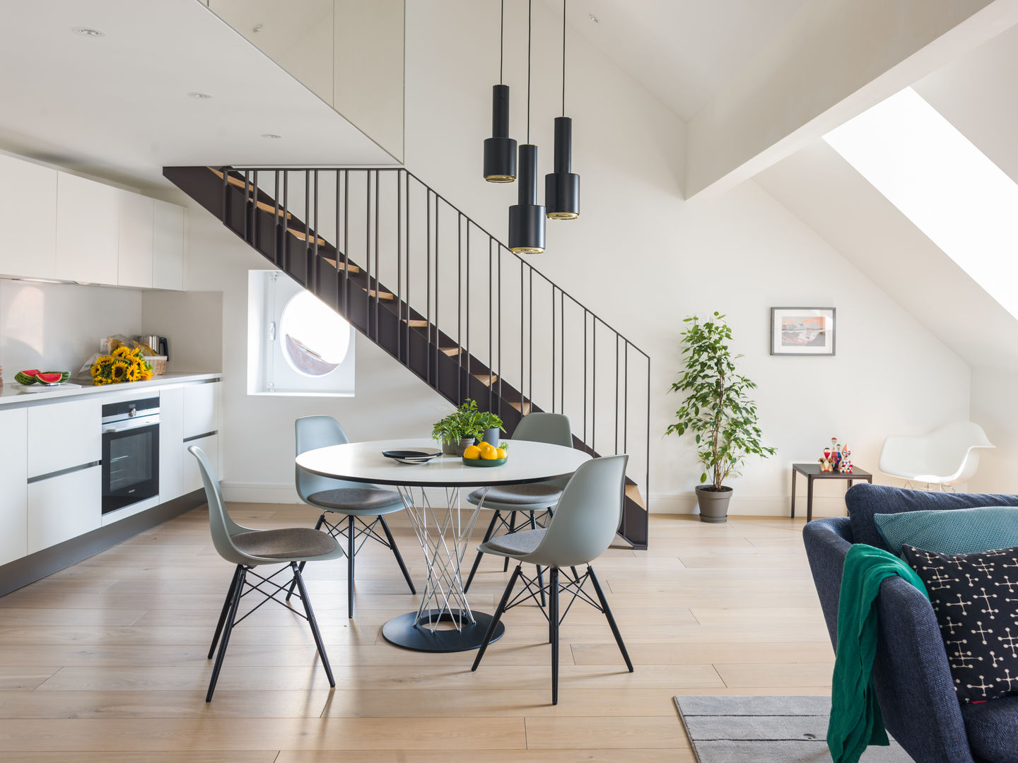 Helle Wohnungseinrichtung mit Esstisch und vier grauen Eames DSW Stühlen mit Sitzpolster von Vitra.