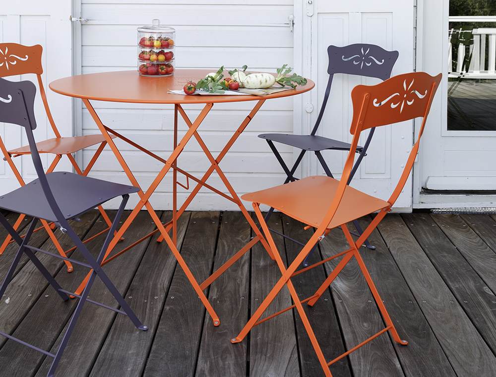 Orangefarbener Fermob Bistro Klapptisch mit passenden Stühlen auf einer Holzterrasse, ideal für den Garten.