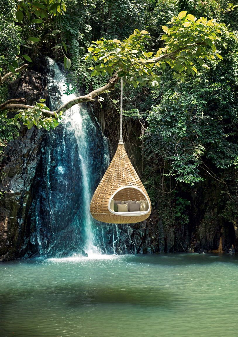 Hängender Rattansessel mit Kissen vor Wasserfall. Gemütliche Hängehöhle für Garten, Terrasse oder Balkon.