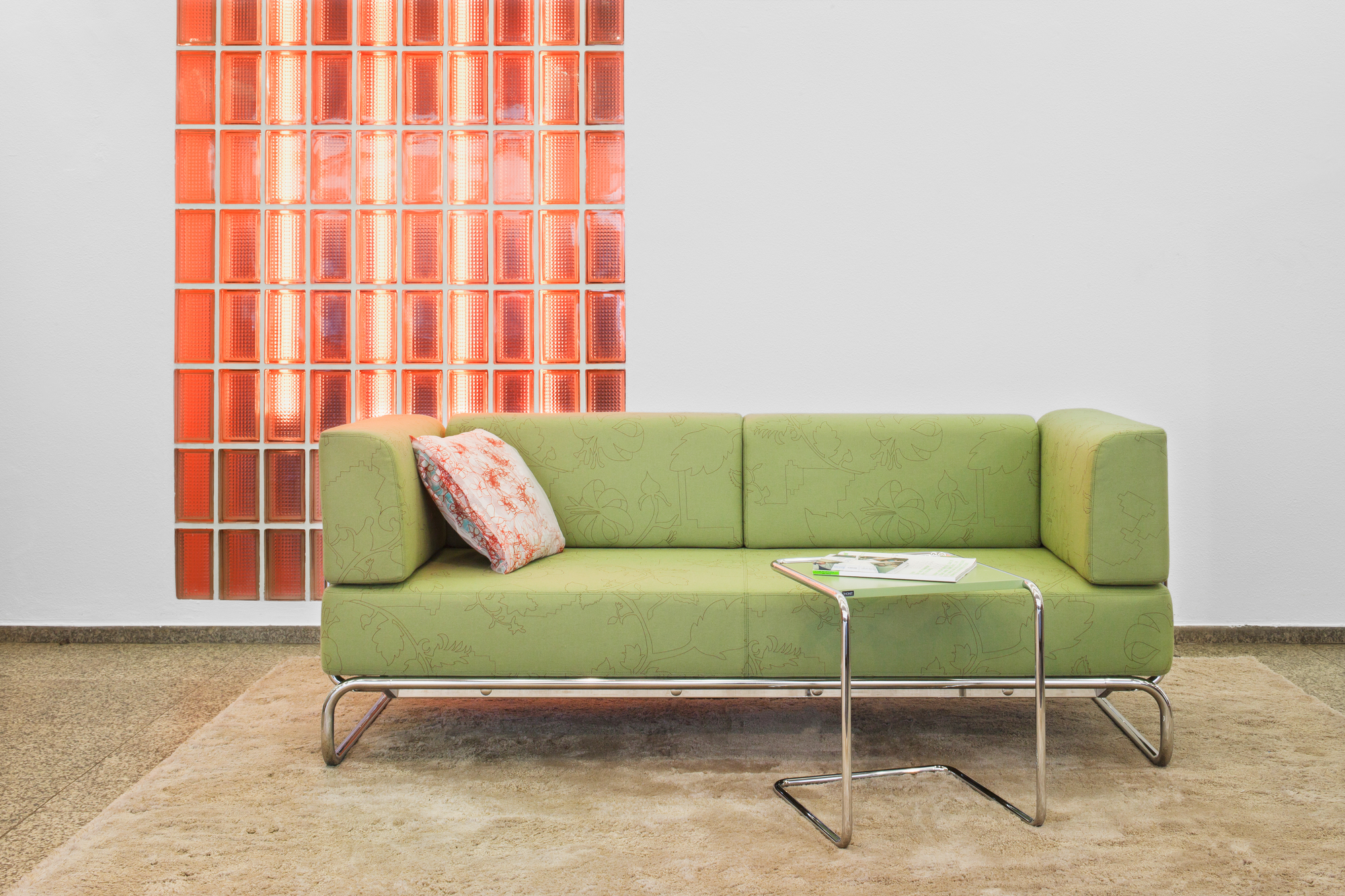 B97 Thonet Beistelltisch aus Stahlrohr neben grünem Sofa mit Kissen und Magazinen auf Teppich.