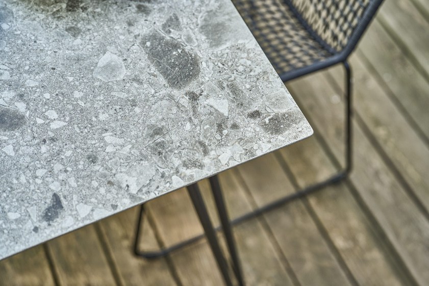 Detailaufnahme der grauen Tischplatte des Slope Tisch Outdoor von Weishäupl mit Stuhl im Hintergrund.
