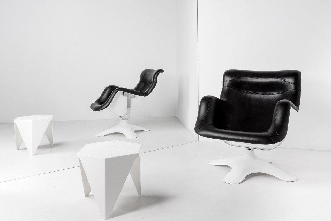 Schwarzer Karuselli Sessel von Artek mit weißem Fuß und zwei weißen Hockern im minimalistischen Raum.