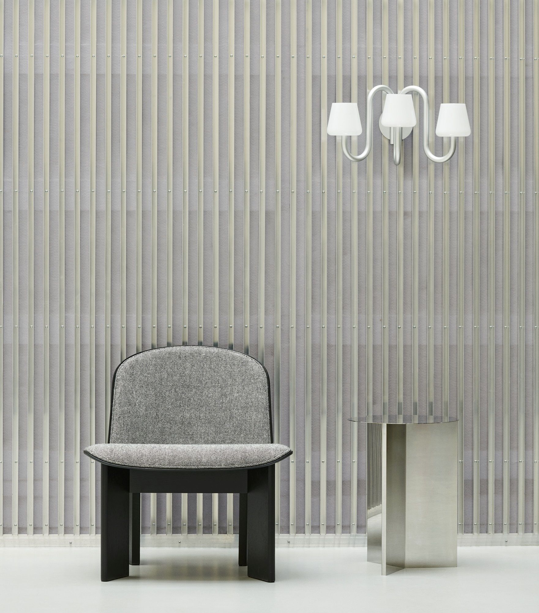 Hay Slit Table Round High Beistelltisch aus poliertem Edelstahl neben einem grauen Sessel und einer Lampe.