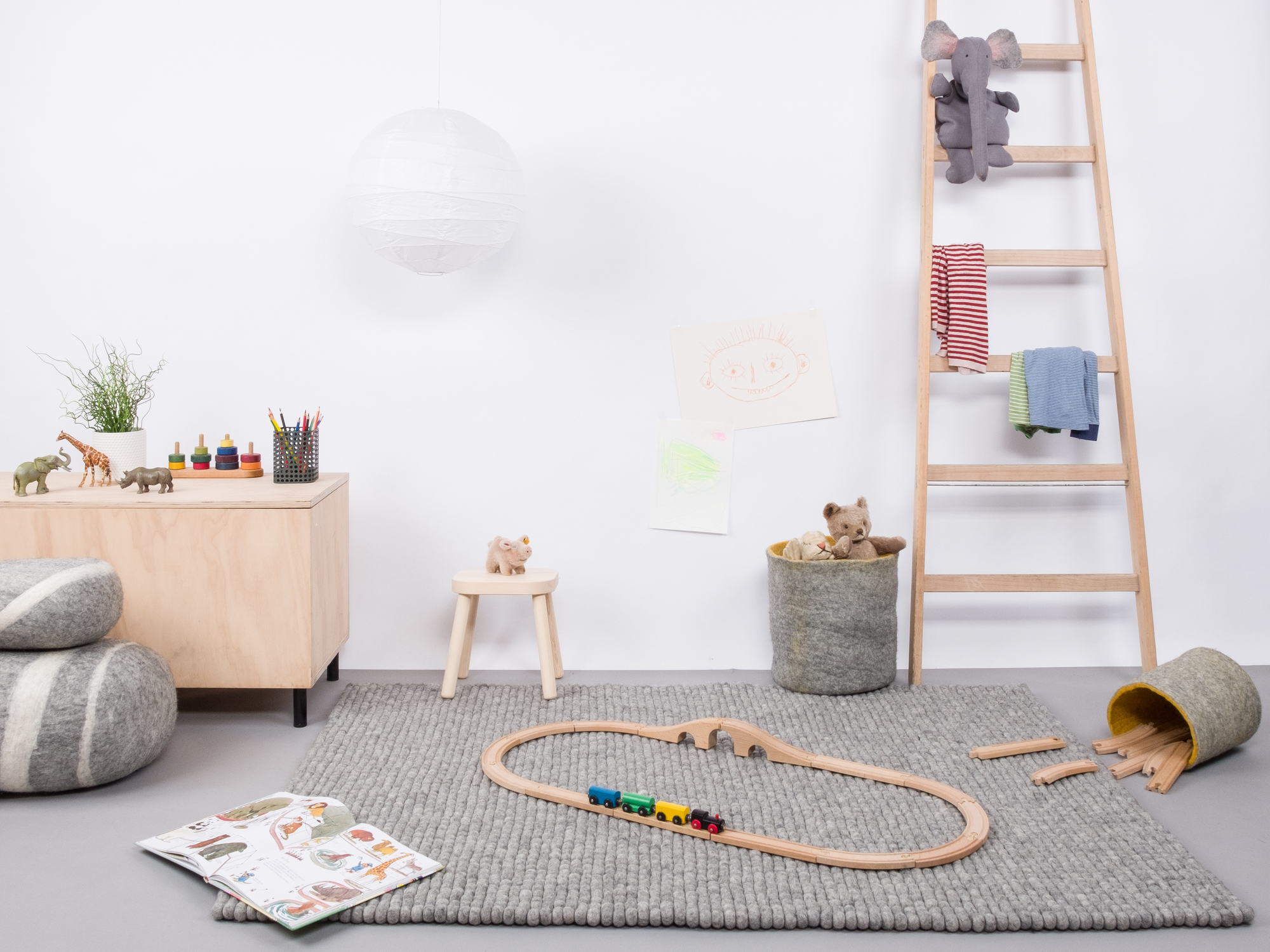Grauer myfelt Filzkugel Teppich 120x170 cm im Kinderzimmer mit Spielzeug und Holzeisenbahn.