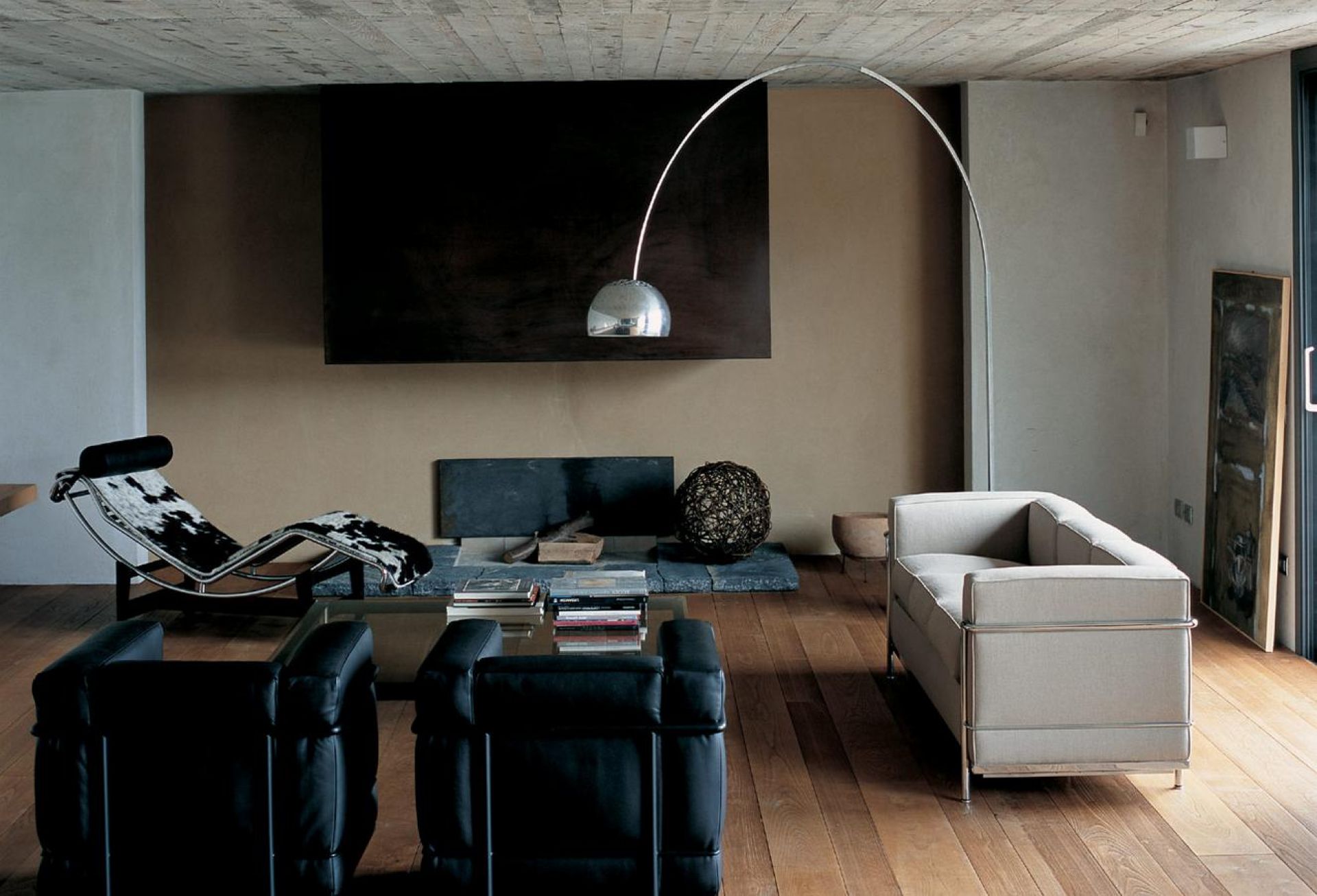 Wohnzimmer mit Designermöbeln: Ledersessel, Liege mit Kuhfell, Bogenlampe und modernem Sofa.
