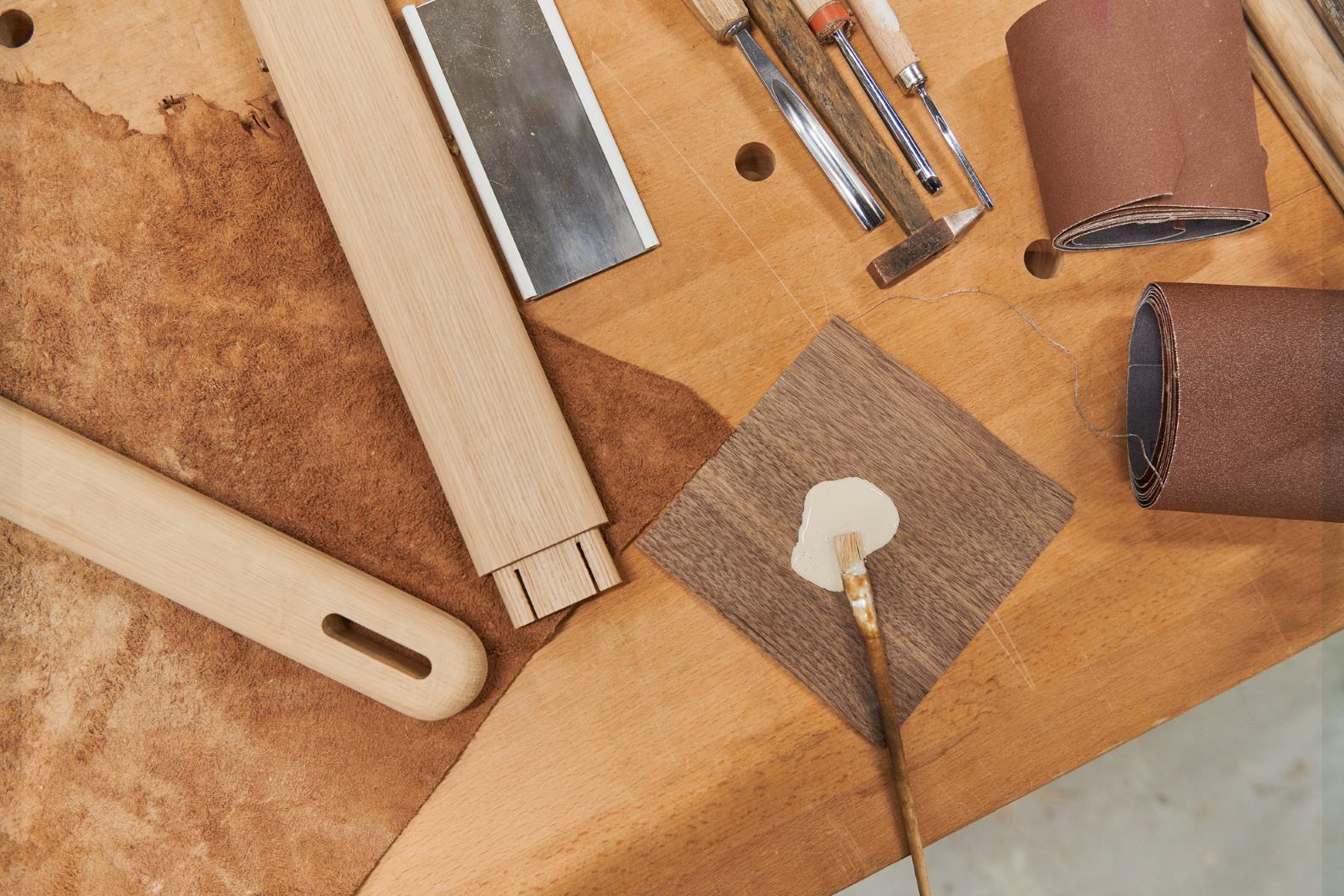 Werkbank mit Holzwerkzeugen: Stecheisen, Schleifpapier, Pinsel mit Kleber und Holzstücke für Möbelbau.