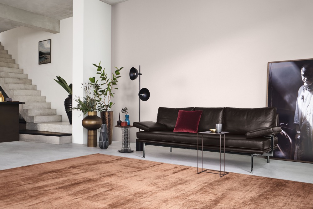Dunkelbraunes LIVING PLATFORM Sofa von Walter Knoll mit Funktionsarmlehnen und rotem Kissen in modernem Wohnzimmer.
