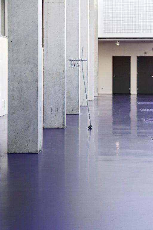 Moderner Garderobenständer aus Metall auf lila Industrieboden zwischen Betonpfeilern in einem minimalistischen Gebäude.