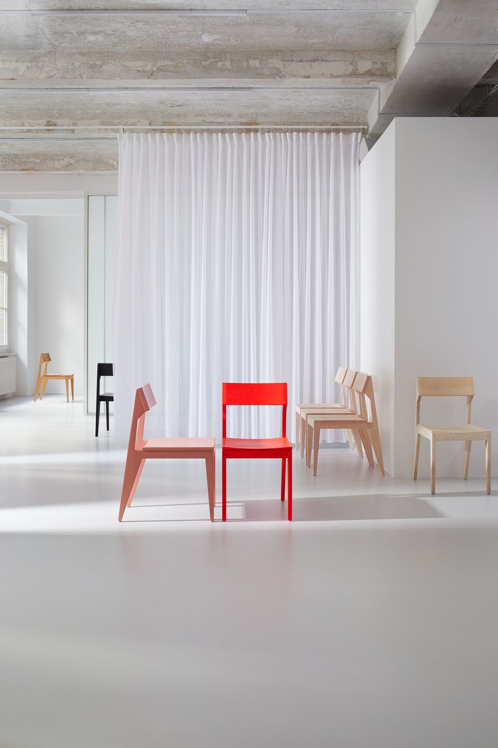 Verschiedenfarbige SCHULZ Stühle OUT in minimalistischem Raum mit weißem Vorhang, moderne Holzstühle für Esszimmer und Wohnbereich.