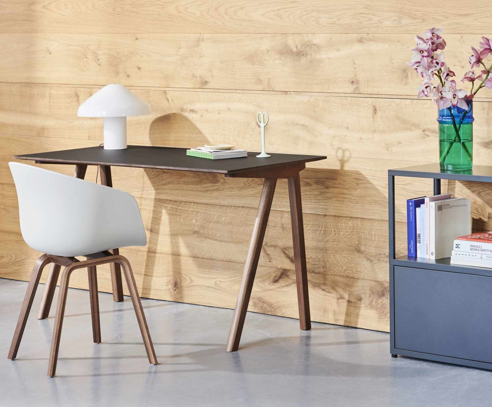 Hay Copenhague Table CPH 90 Schreibtisch mit Lampe, Stuhl und Dekoration vor einer Holzwand.