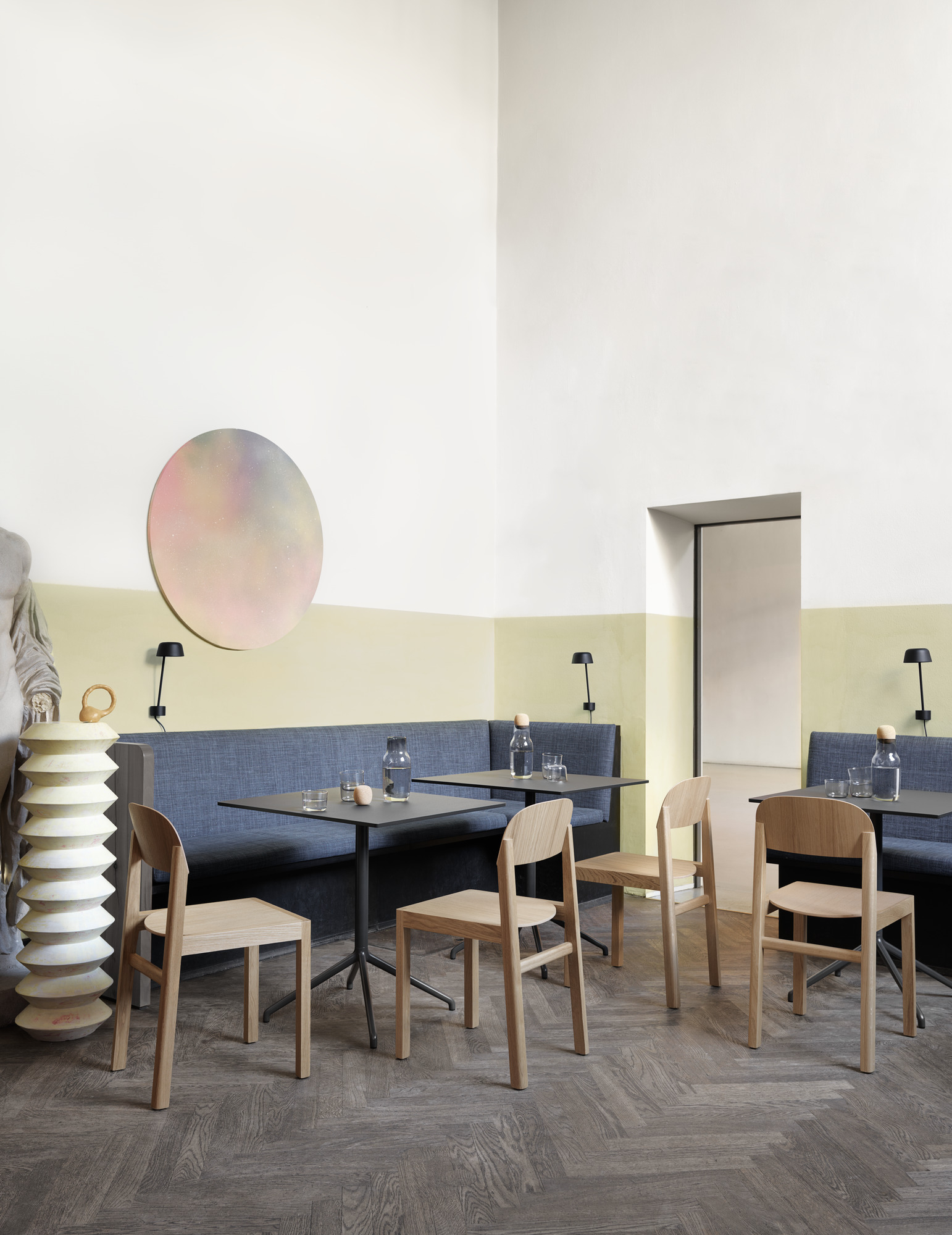 Innenaufnahme eines Cafés mit Muuto Still Cafe Tischen und Holzstühlen an einer blauen Sitzbank.