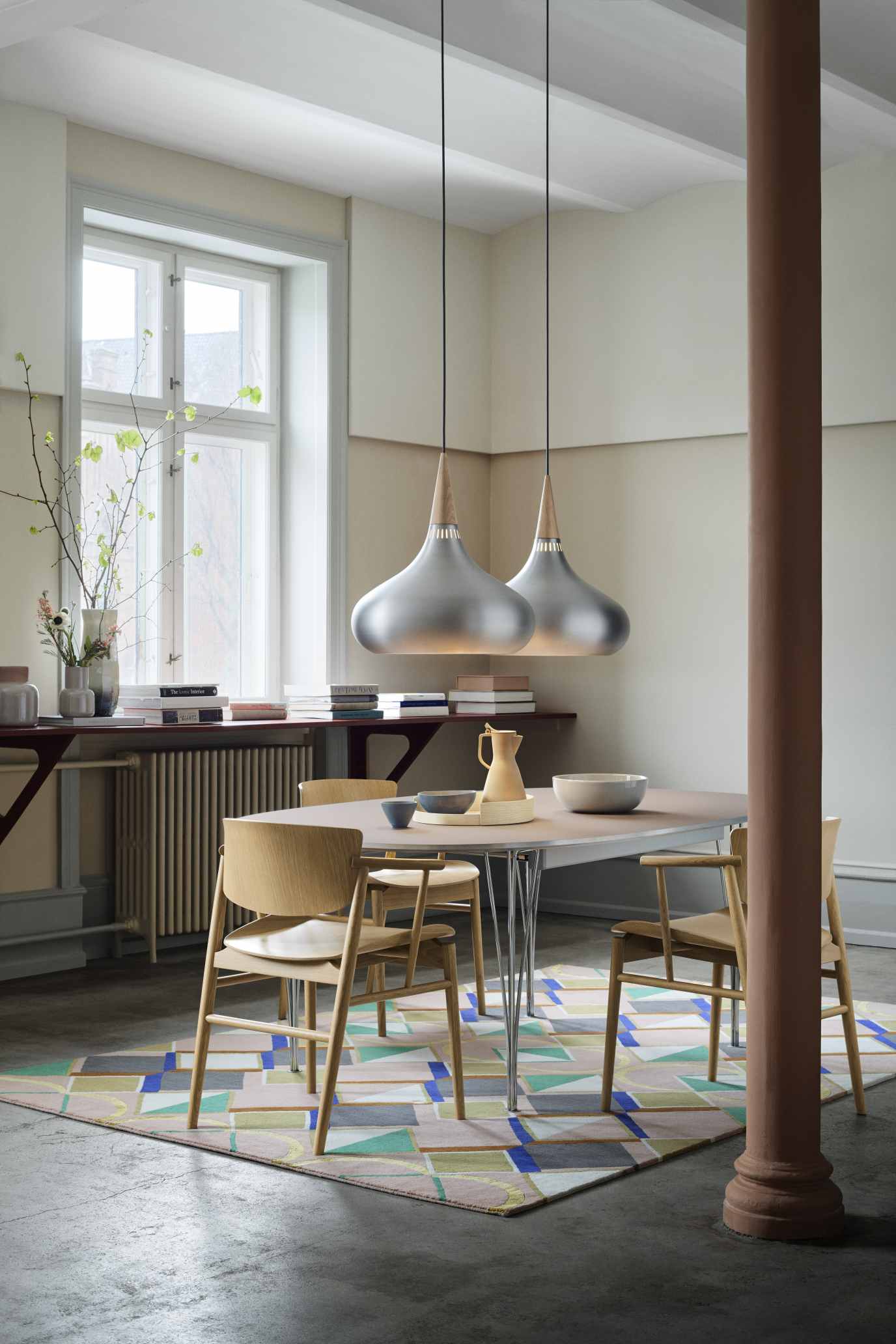Fritz Hansen Super Elliptisch Ausziehtisch mit Holzstühlen und zwei Pendelleuchten in einem hellen Esszimmer.