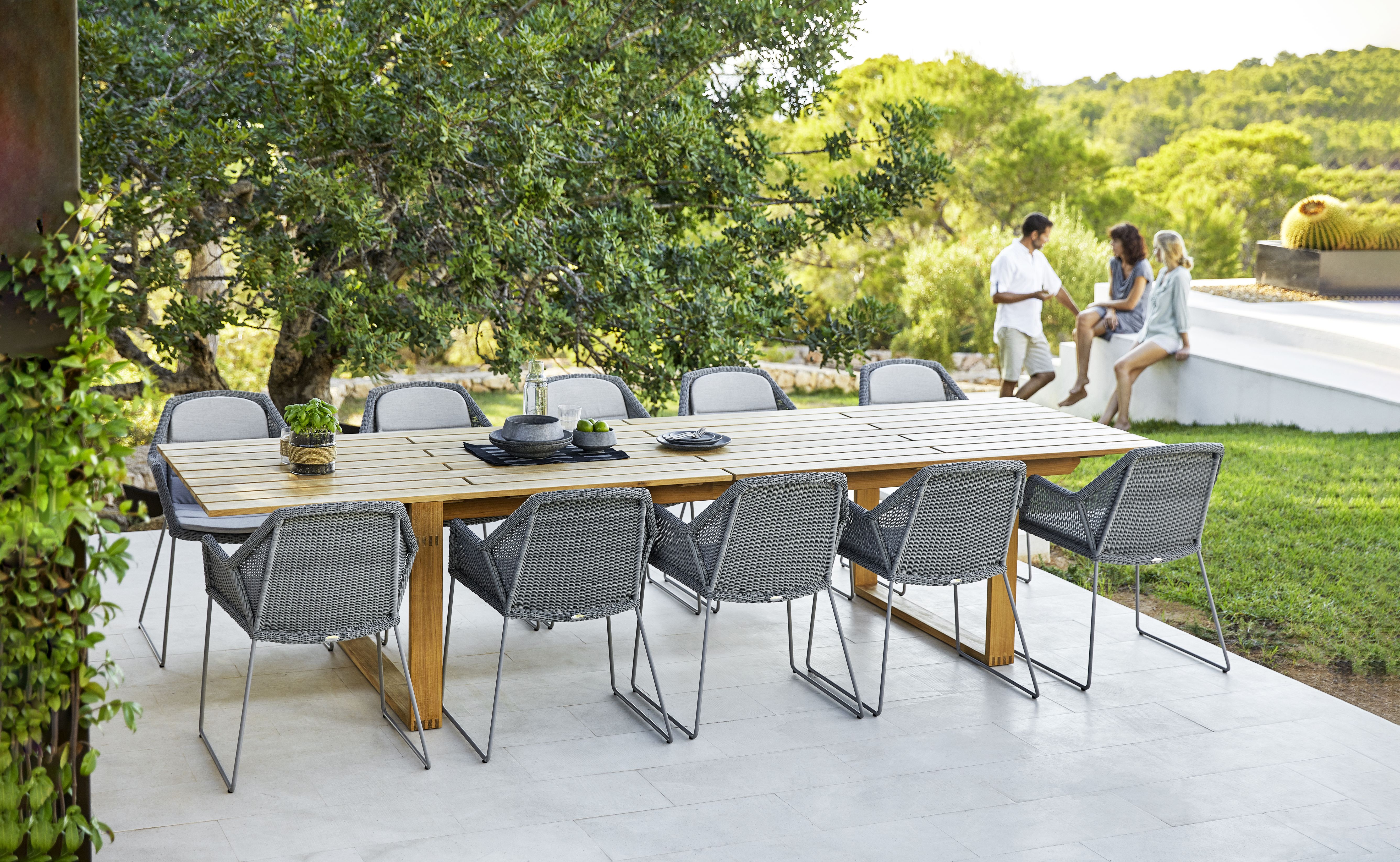 Endless Esstisch von Cane-Line: Rechteckiger Gartentisch aus Teakholz mit grauen Korbsesseln im Außenbereich.