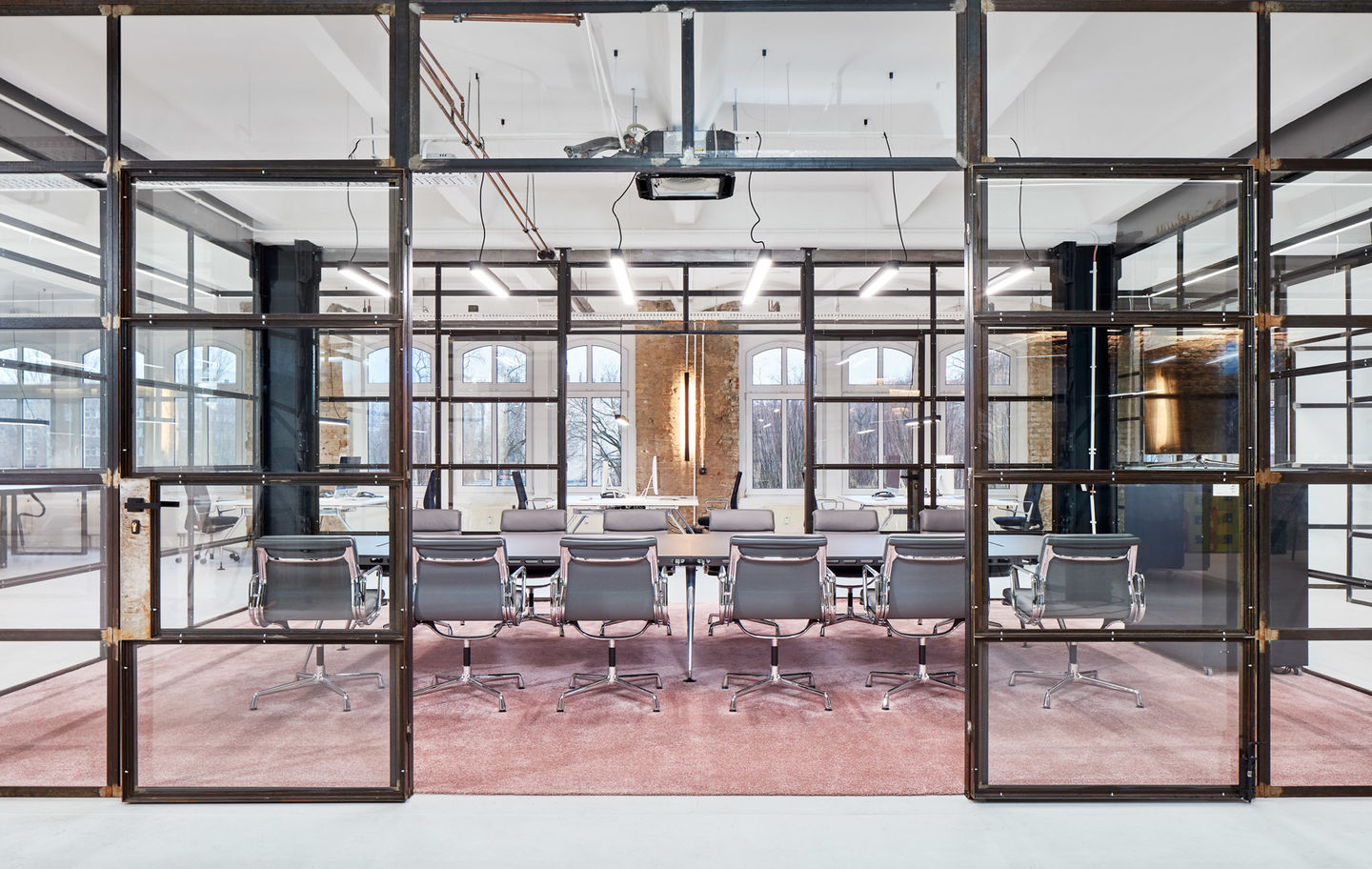 Konferenzraum mit Soft Pad Chair EA205 von Vitra, graue Ledersessel an langem Tisch auf rosa Teppich.