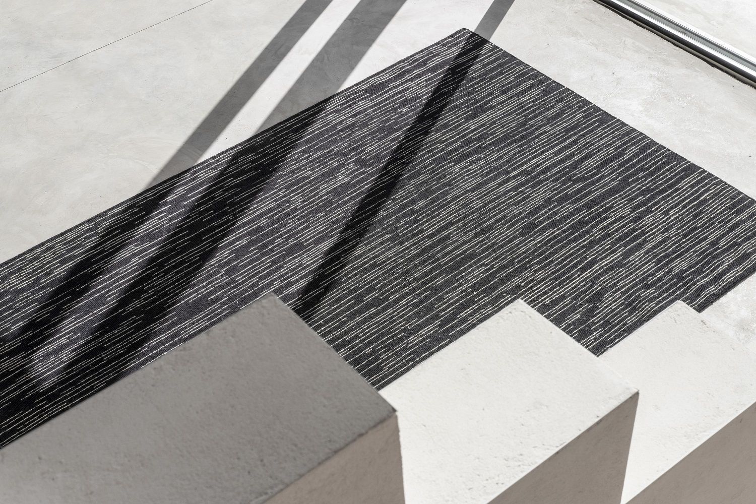 Detailaufnahme des Nanimarquina Doblecara Rug Teppichs in Schwarz-Weiß auf einer Betontreppe.