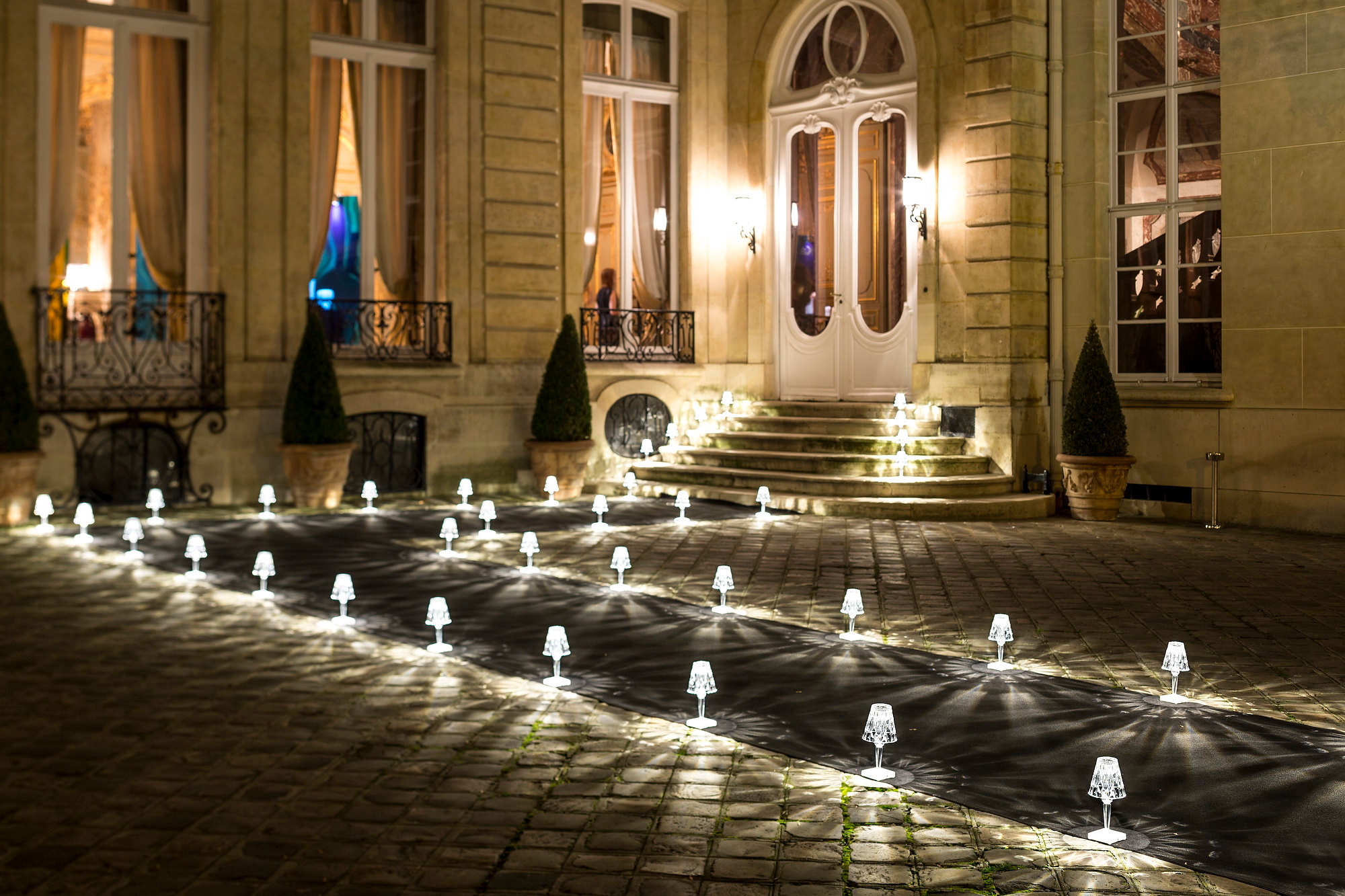 Battery Tischleuchte von Kartell, rauchfarben, beleuchtet einen Weg vor einem Gebäude. Dekorative LED Lampe.