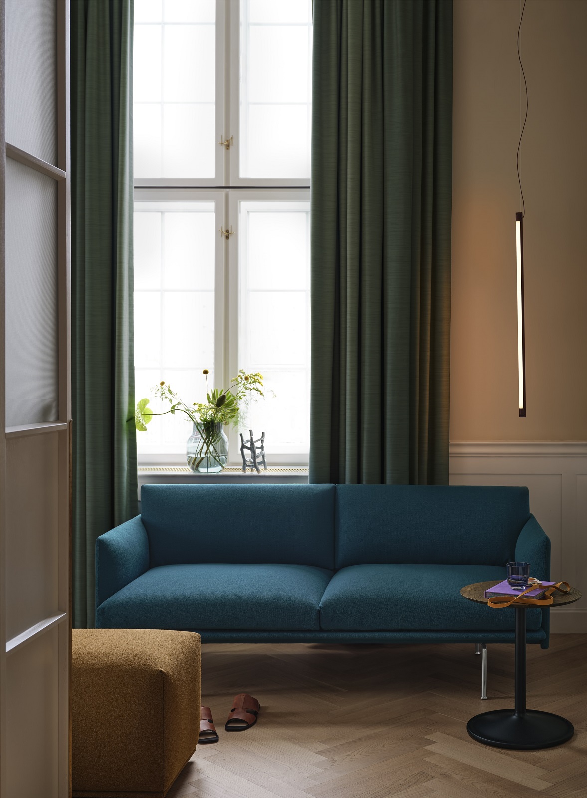 Wohnzimmer-Szene mit blauem Sofa, kleinem Beistelltisch, Stehlampe und senffarbenem Echo Pouf Hocker von Muuto.