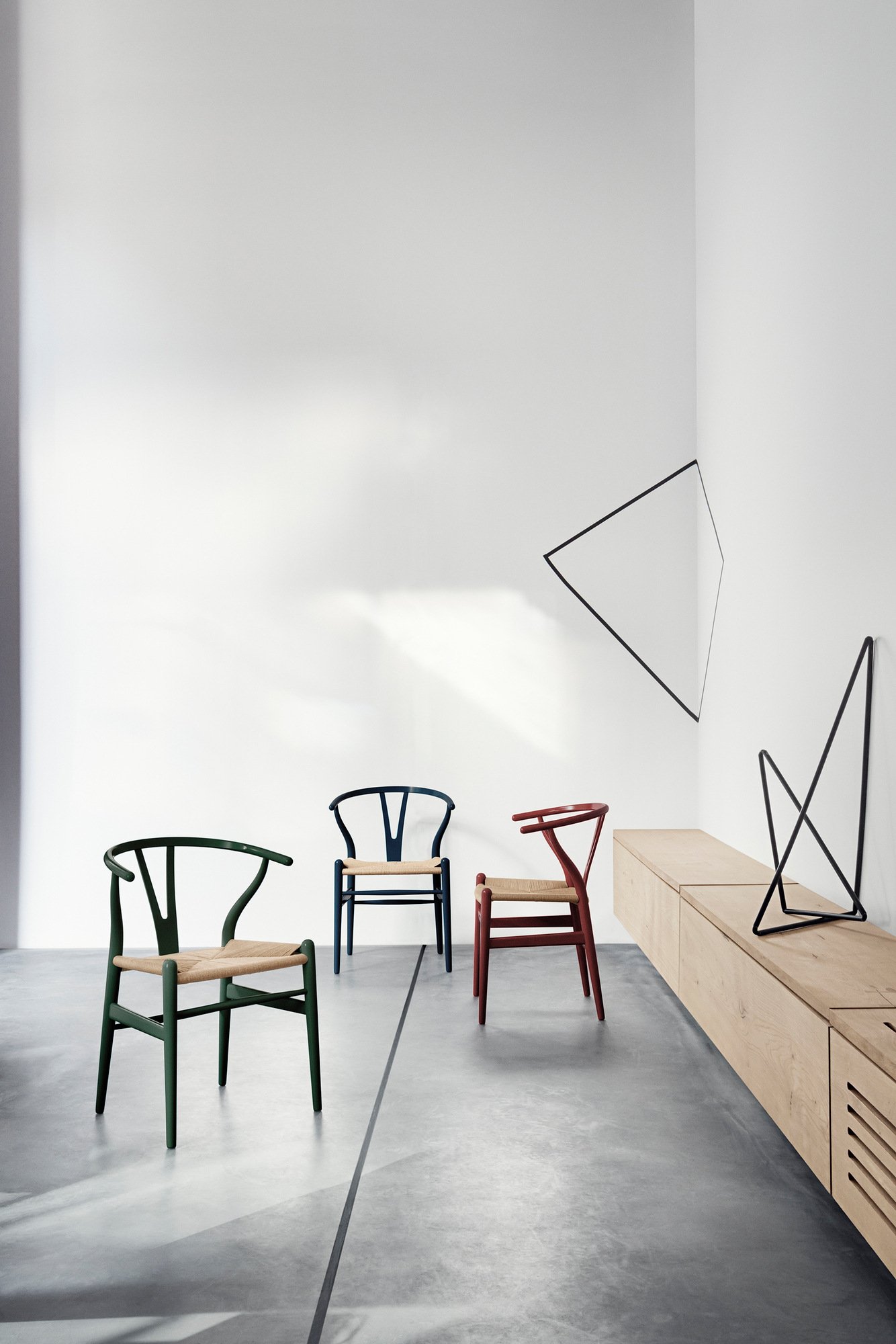 Drei CH24 Wishbone Stühle in Grün, Blau und Russet mit geflochtenen Sitzen in minimalistischem Interieur.