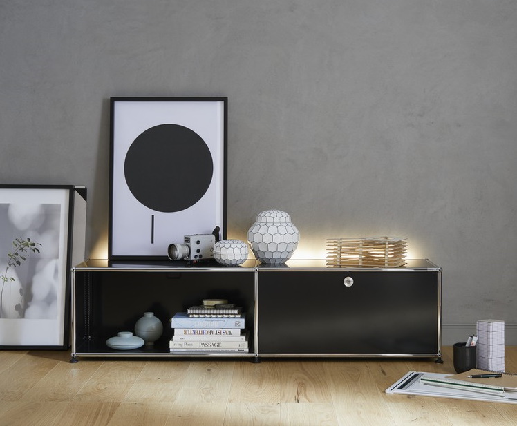 Schwarzes Sideboard mit Chromgestell, dekoriert mit Bildern, Kamera und Deko-Objekten im modernen Wohnzimmer.