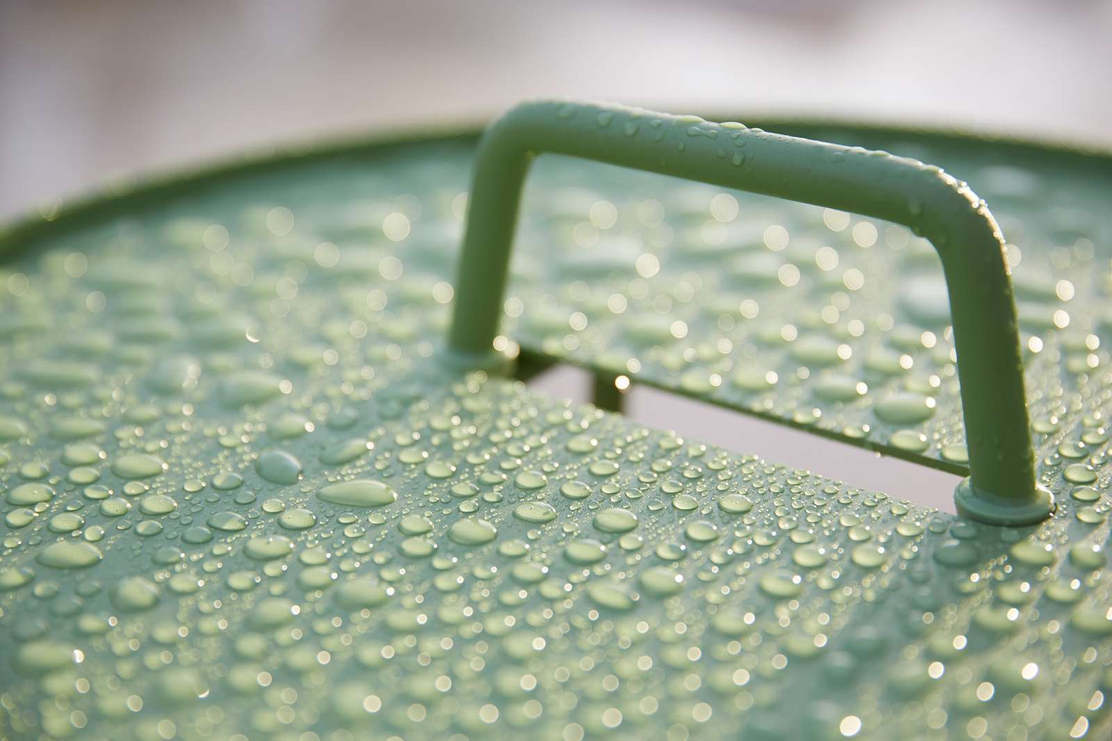 Nahaufnahme des grünen Cane-Line On-The-Move Beistelltisches im Freien mit Wassertropfen nach einem Regenschauer.
