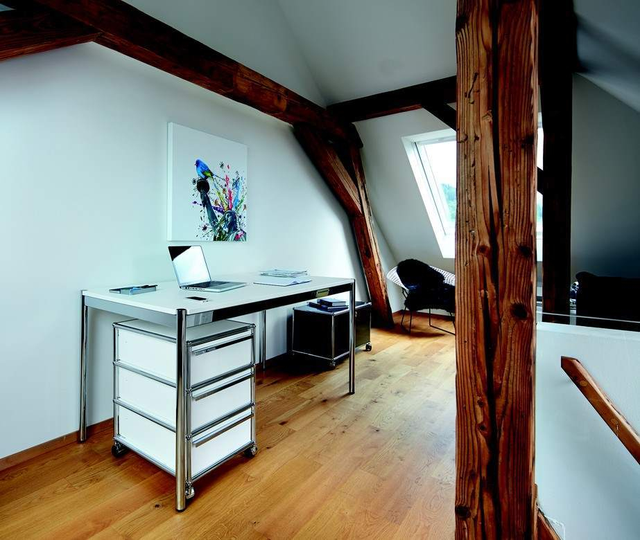 USM Haller Rollcontainer in Weiß unter Schreibtisch in Dachgeschossbüro mit Holzbalken und Parkettboden.
