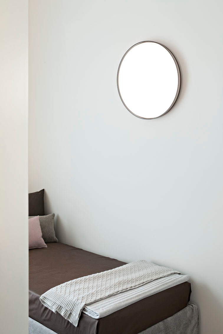 Minimalistische Clara Wandleuchte von Flos über einem Bett, modernes Design mit runder Form.