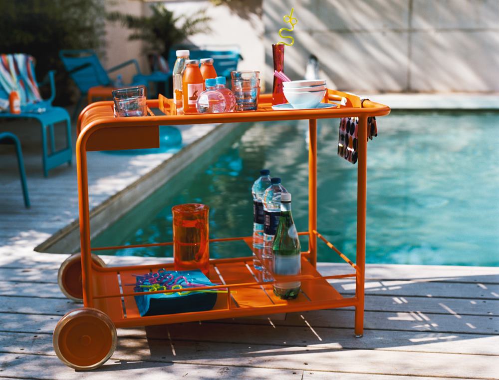 Orangefarbener Fermob Luxembourg Servierwagen im Freien am Pool mit Getränken und Geschirr.