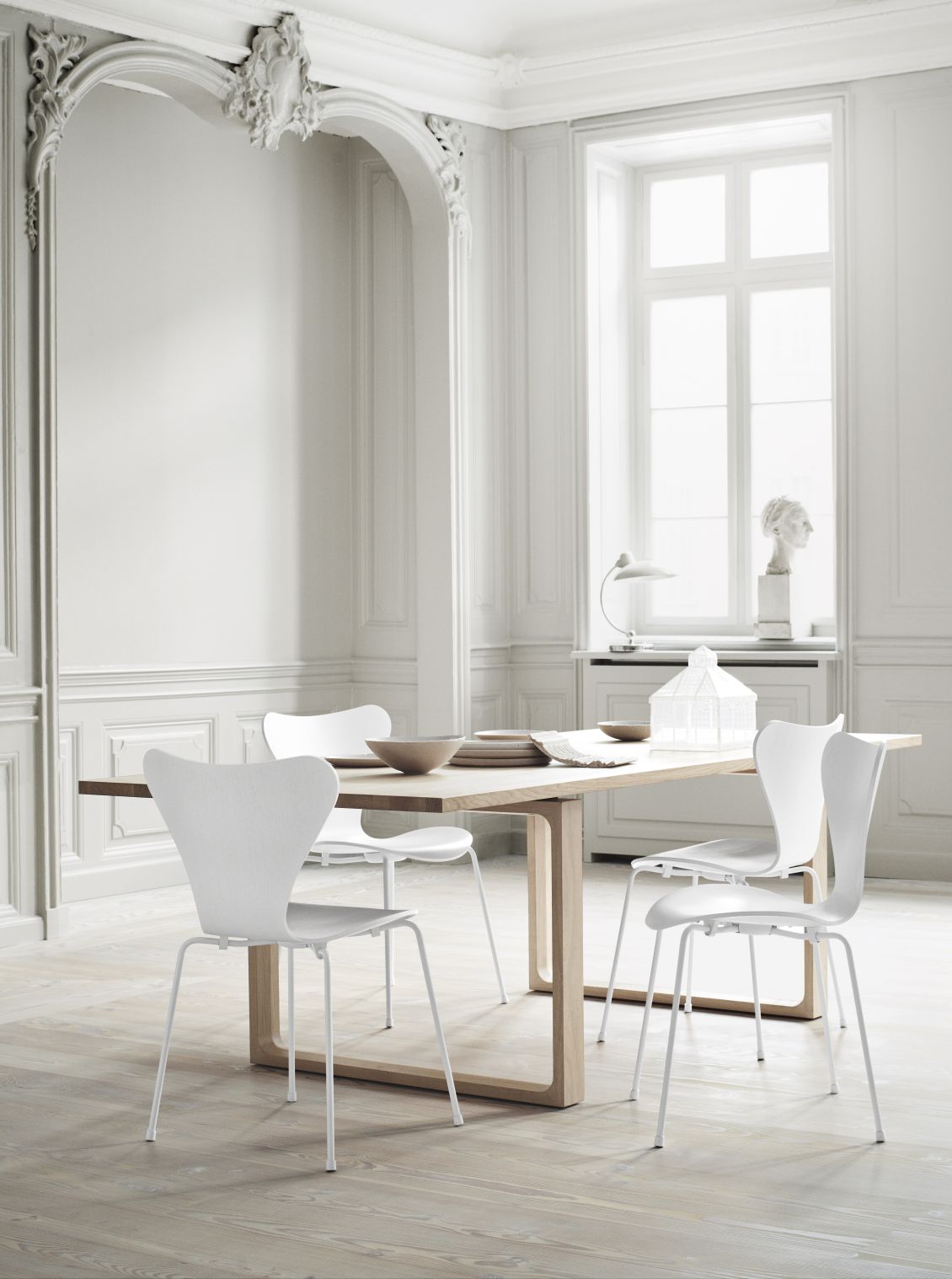 Heller Raum mit Fritz Hansen Essay Tisch aus Holz und weißen Stühlen, Essteller und Schalen.