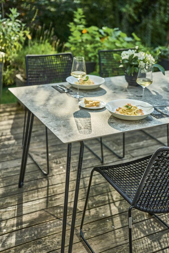 Slope Tisch von Weishäupl, graue Tischplatte, schwarzes Gestell, gedeckt mit Pasta und Wein im Garten.