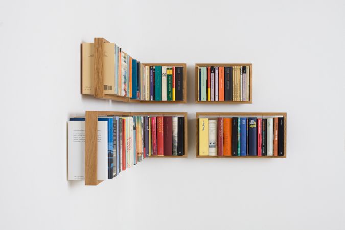 Wandmontiertes Regal b Eiche, bestehend aus vier kleinen Holzregalen mit Büchern an einer weißen Wand.